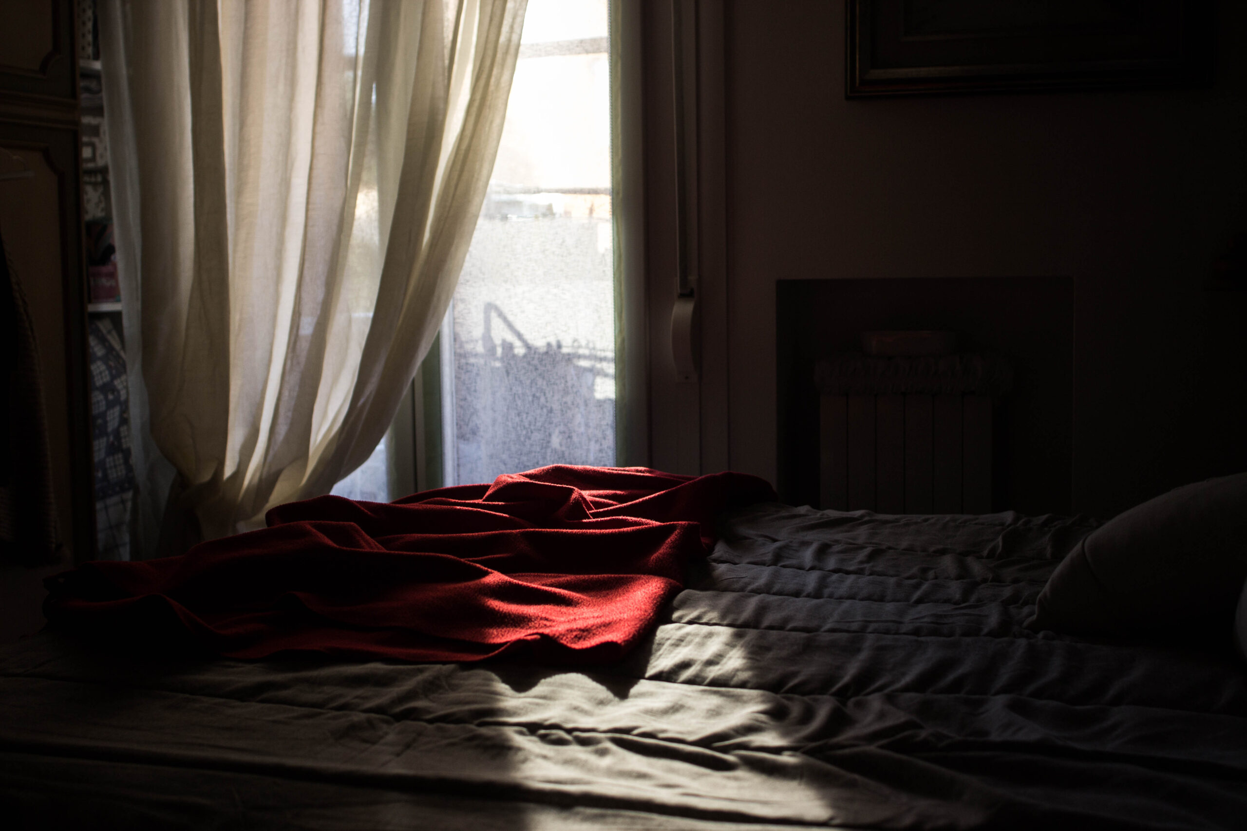 fotografia: un letto con una coperta rossa illuminata da un fascio di luce